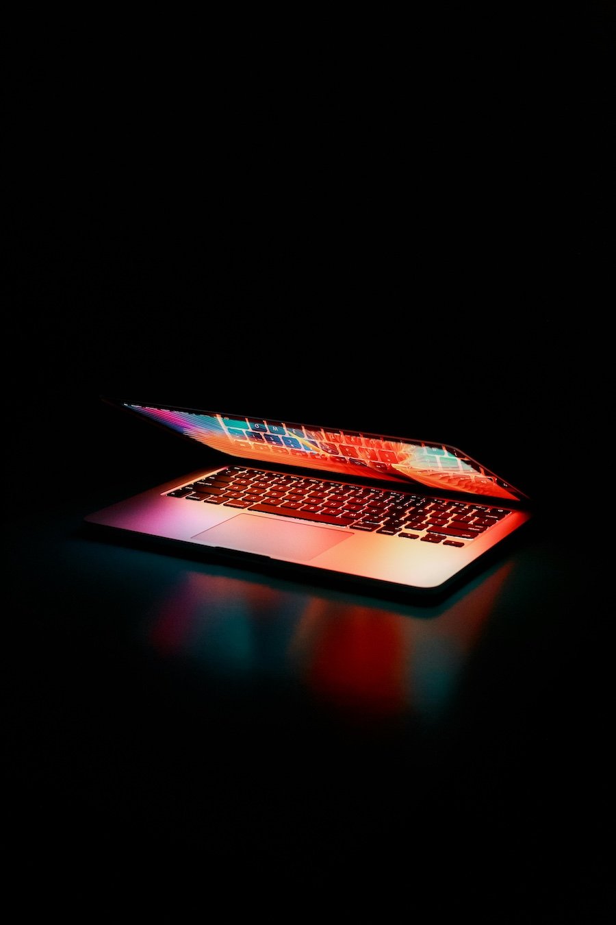 Partially open laptop with colorful screen against a dark black backdrop.